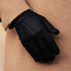 Dark leather glove resting on tan coat sleeve, showing stitched back panel