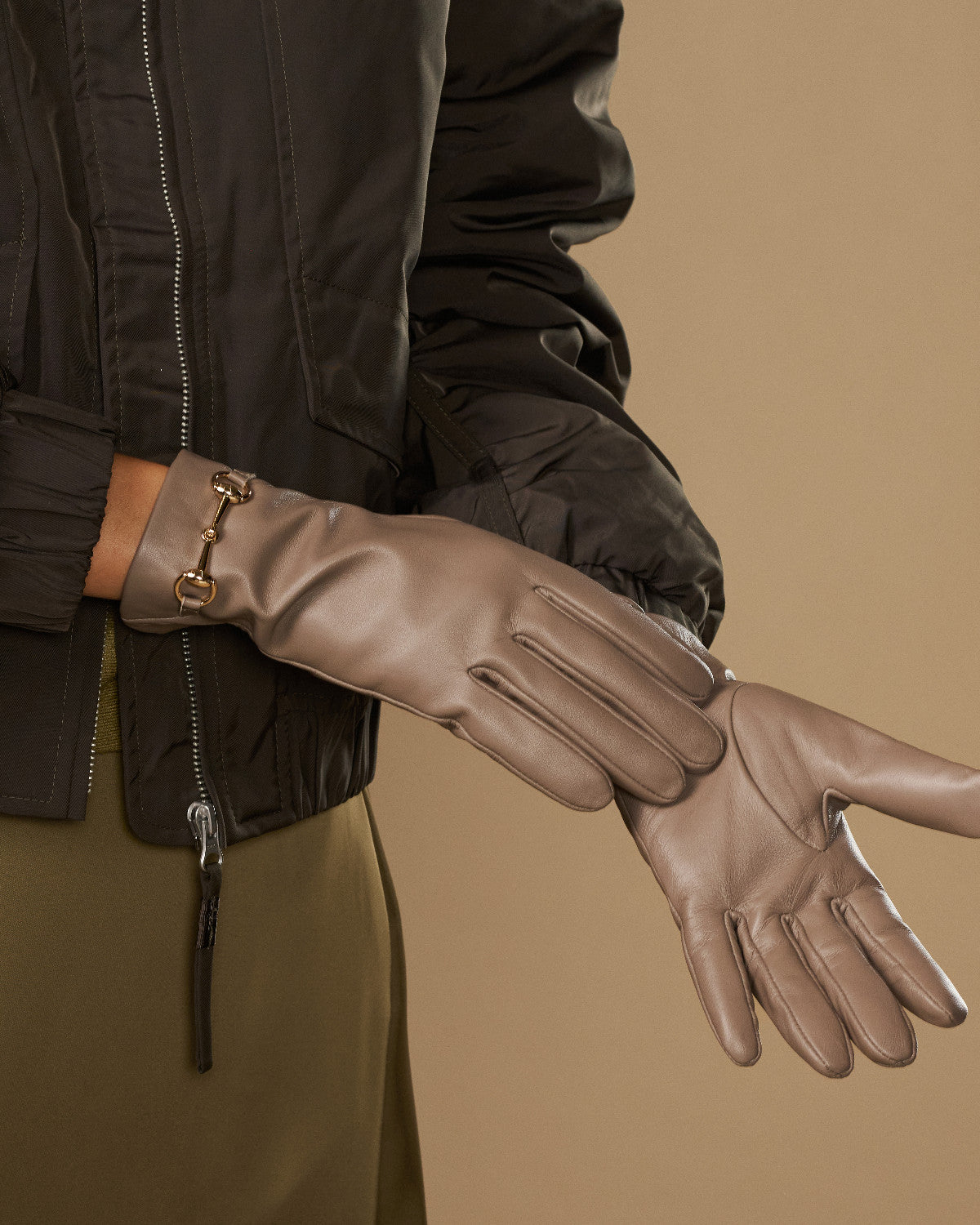Taupe leather glove close-up with gold-tone buckle wrist strap and stitching lines