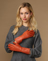 Orange leather gloves on hands with long cuffs and snug fit at wrists