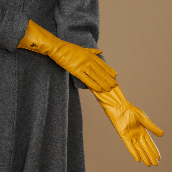 Yellow extra-long leather gloves stretched forward; cuff logo and seam details