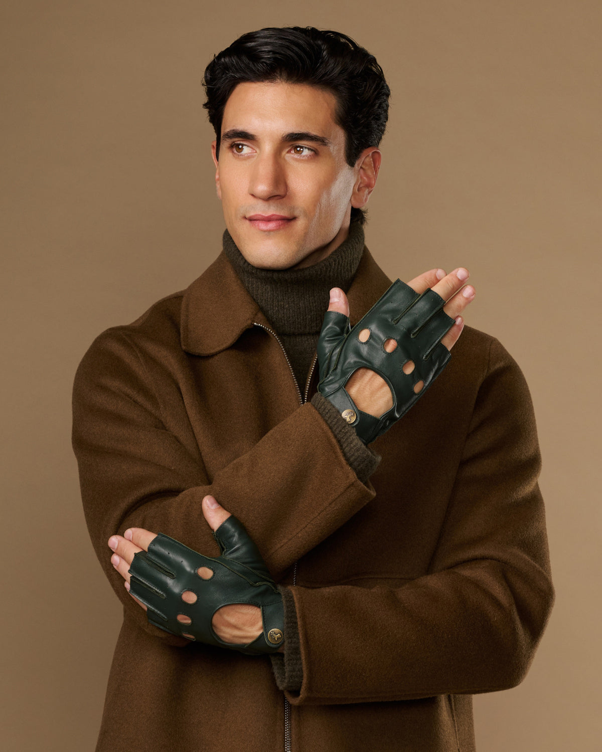 Dark green fingerless driving gloves with perforated knuckles and wrist openings, worn on both hands
