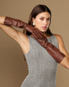 Women's brown below-elbow leather gloves with silk lining, one glove stretched forward