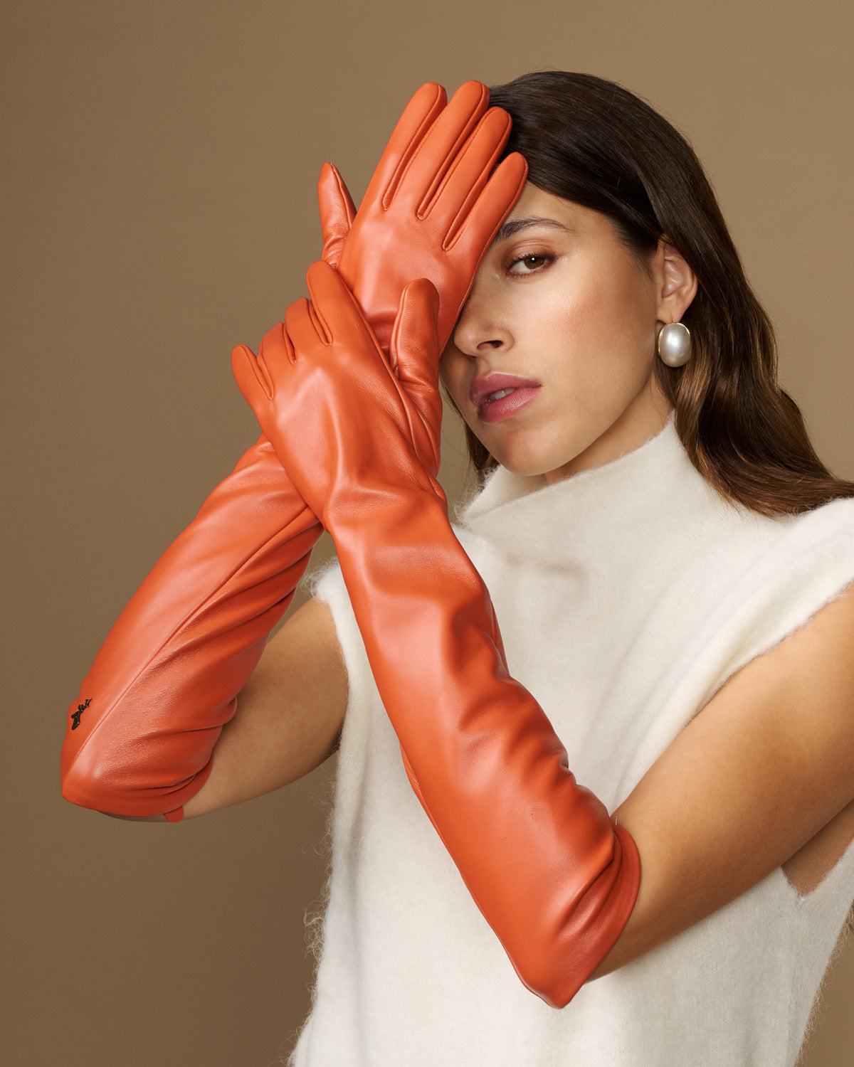 Close-up of orange leather elbow gloves with smooth, glossy finish and finger details